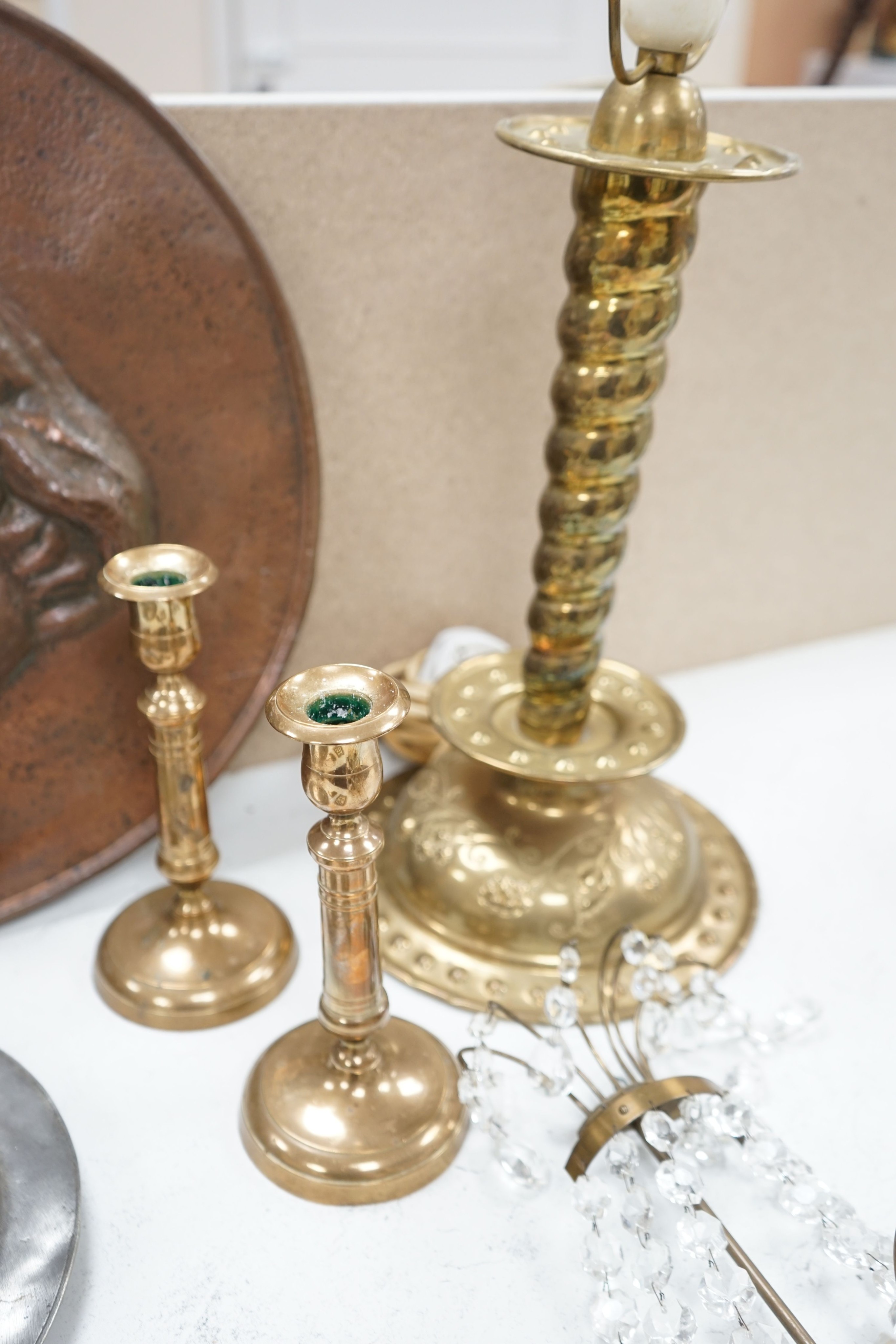 An embossed brass lamp, lustre drop wall light, a pair of bell-metal candlesticks, an 18th century pewter plate and a large Swedish embossed plaque